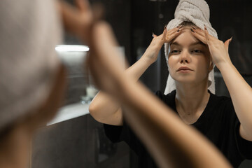 beautiful woman with a towel on her head applies cream to her face in the bathroom