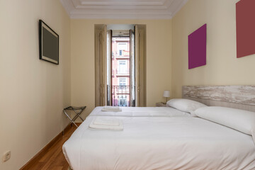 bedroom with two beds together with white bedding, wooden headboard and white lacquered carpentry, balcony with wooden shutters and parquet floor in vacation rental apartment