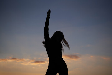 Dancing silhouette of attractive caucasian elegant girl at sunset or woman performing modern dance...