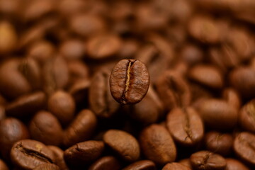 Side view on natural roasted coffee bean hovering on blurry background of coffee beans close up. Selective soft focus, twisted bokeh effect