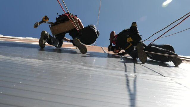 Two construction workers hanging on a building repairing the facade from below