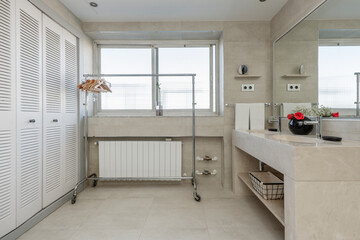 Bathroom with cream colored marble sink with frameless mirror, white aluminum radiator and cabinet with Venetian doors