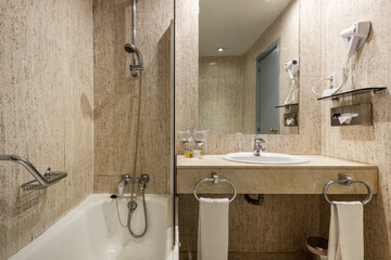 bathroom with marble sink and matching marble-clad floors and walls with shower and frameless wall mirror, towel racks with fresh towels and wall-mounted hairdryer
