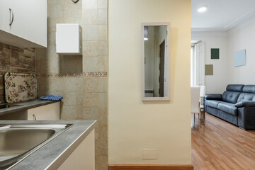 Stainless steel sink in a small kitchen open to a living room with parquet flooring and a...