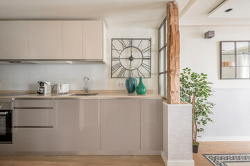 Kitchen open to a living room with restored wooden columns, gray lacquered furniture and decorative plants