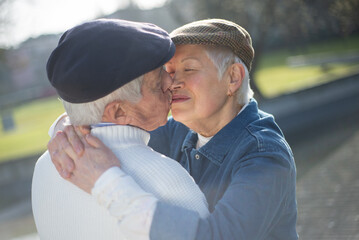 Close-up of senior couple kissing in spring park. Grey-haired man and woman hugging and kissing when walking in city recreation zone. Active rest, relations and love of aged people concept