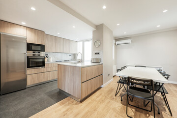 Open plan kitchen with oak cabinets, island with white marble top and dining table with eight black folding chairs