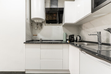 Corner of a kitchen with a black countertop and white cabinets with small appliances on the countertop