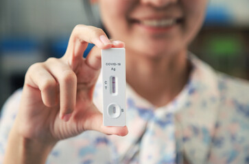 smiling girl showing ATK test result from home testing before doing daily life activity. selective focus.