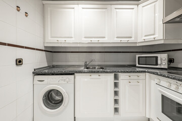 Corner of a kitchen with a simil black quartz countertop and white cabinets with a white microwave oven and small appliances on the countertop