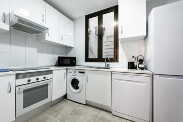 Corner of a fully fitted white kitchen with matching white appliances and ceramic tile flooring