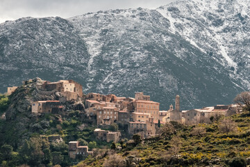 Fototapeta na wymiar The village of Speloncato in the Balagne region of Corsica with snow capped mountains behind