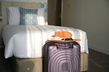 The purple suitcase has an orange sombrero and a white mask placed on top. A suitcase placed beside a white bed in the hotel room. Tourists must use face masks during  COVID-19 outbreak or has PM2.5

