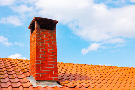 Brick chimney on the rooftop and partly cloudy sky on the background