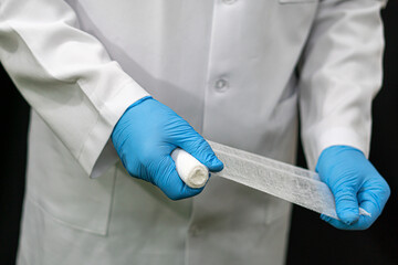 A young traumatologist holds a white medical bandage in his hand. A doctor in a white coat and a bandage in his hands on a black background.