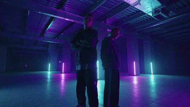 A duet of two professional dancers, a man and a woman. A stylish couple dances hip-hop freestyle together in synchronously in lard lit in blue purple hues with neon light