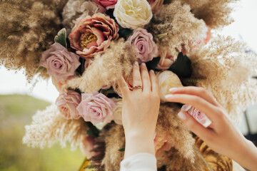 Hands of the bride close-up. Ring of gold on the finger of bride on the background of roses and pampas grass.