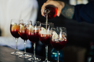 Professional barman pours alcoholic drink into glasses with one hand.