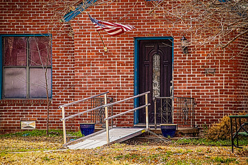 Metal handicap ramp built out from front porch of brick house with American flag flying on winter...