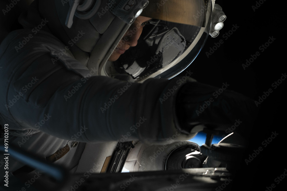 Wall mural female astronaut performing spacewalk, working on a outer part of a space craft