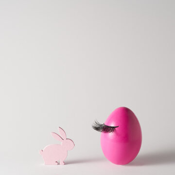 Pink Easter egg with false eyelashes and pastel pink bunny on grey background. Beauty and make up concept. Spring, Easter minimal design. Copy space for text.