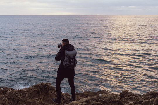 Tourist taking a picture on the cliffs of Boca do Inferno at sunset