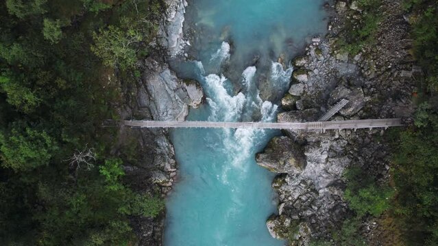 Aerial drone zoom in shot of aesthetic suspension old wooden bridge over epic mountain rocks and waterfall river. Scandinavian or northern hiking culture. Healthy adventure in outdoors