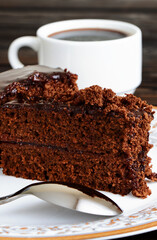 A piece of Chocolate cake on a plate and cup of black coffee on a wooden background.Slice of Homemade brownie cake. Vertical orientation