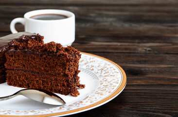 A piece of Chocolate cake on a plate and cup of black coffee on a wooden background.Slice of Homemade brownie cake.Copy space