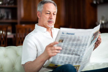 Senior man at home reading newspaper