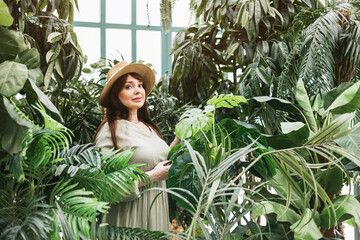 young woman plus size model in long green summer dress in greenhouse with tropical plants and...