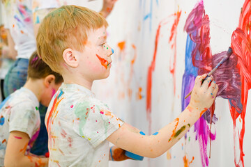 Little children draw with colorful paints on white walls . High quality photo