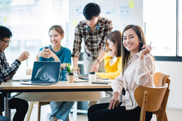 A positive secretary smiles for the camera during a meeting with colleagues working in the background.