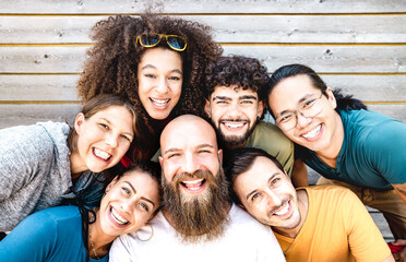 Multicultural guys and girls taking selfie outdoors on wooden background - Happy milenial life style concept with young multiethnic hipster people having fun day together - Warm bright filter - obrazy, fototapety, plakaty