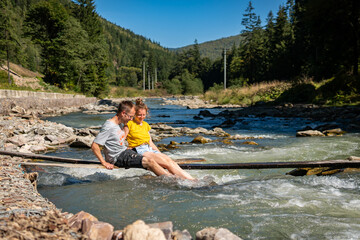 A lovely couple is enjoying time together on a thin desk over a river in the mountains
