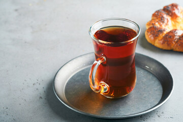 Turkish black tea. Glass cup of turkish black tea and crispy Turkish traditional bagel on gray concrete table background. Breakfast pastry concept. Traditional turkish brewed hot drink.