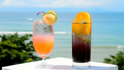 Two tropical cocktails on table with sea view for summer vacation. Two glasses with cocktails and blurry ocean beach on background. Vacation, travel, weekend, holidays concept