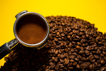 Coffee holder placed into coffee roasted beans on the yellow table in daylight