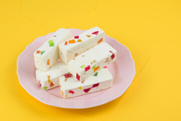 A delicate souffle lies on a plate on a yellow background. A white cake with colored marmalade is lying. A few pieces of sweet delicious pastille.