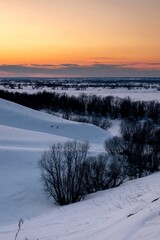 A beautiful view from the top of the hill at sunset over a snowy area with trees. vertical image