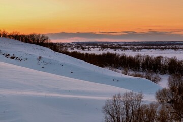 Sunset over snow-covered hills with trees on the slopes. dramatic sky
