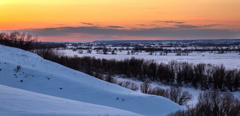 Sunset over snow-covered hills with trees on the slopes. panoramic image
