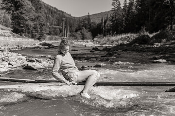 A young woman is enjoying time on a thin desk over a river in the mountains