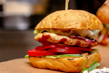 A burger with fried chicken breast, tomatoes and cucumbers lies on a wooden board