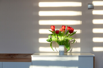Red tulips in a vase on the shelf at home. Bouquet for Mothers day, home decoration	