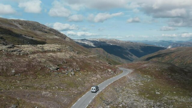 Scenic dramatic drone flight view on adventure inspiring van on beautiful scandinavian mountain travel road trip. Stunning footage of travel, family drives in camper through the rocks, snow in norway.