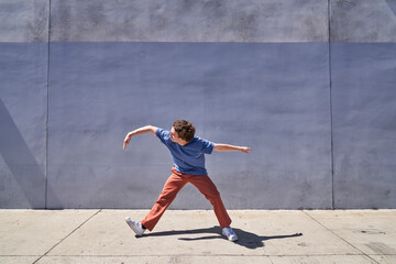 Man doing arm wave in front of gray blue wall	
