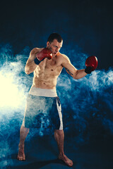 Full length muscular kickbox or muay thai fighter who punching on smoke background. Sport concept.