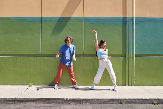 man and woman dancing and posing in front of multicolor wall	
