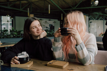 Interracial lesbian couple each other with shy smile, holding hands during lunch at restaurant.